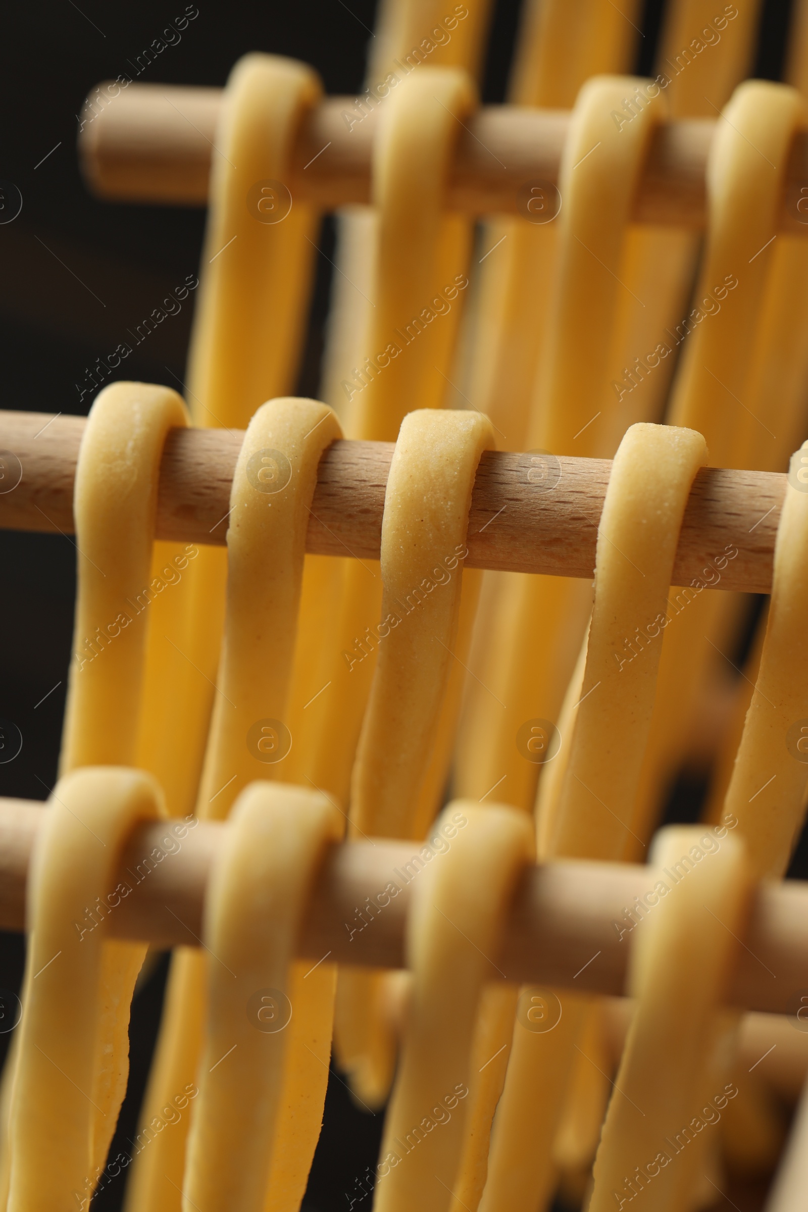 Photo of Homemade pasta drying on wooden rack against dark background, closeup