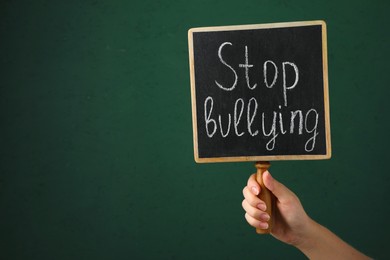 Woman holding chalkboard with phrase Stop Bullying on green background, closeup