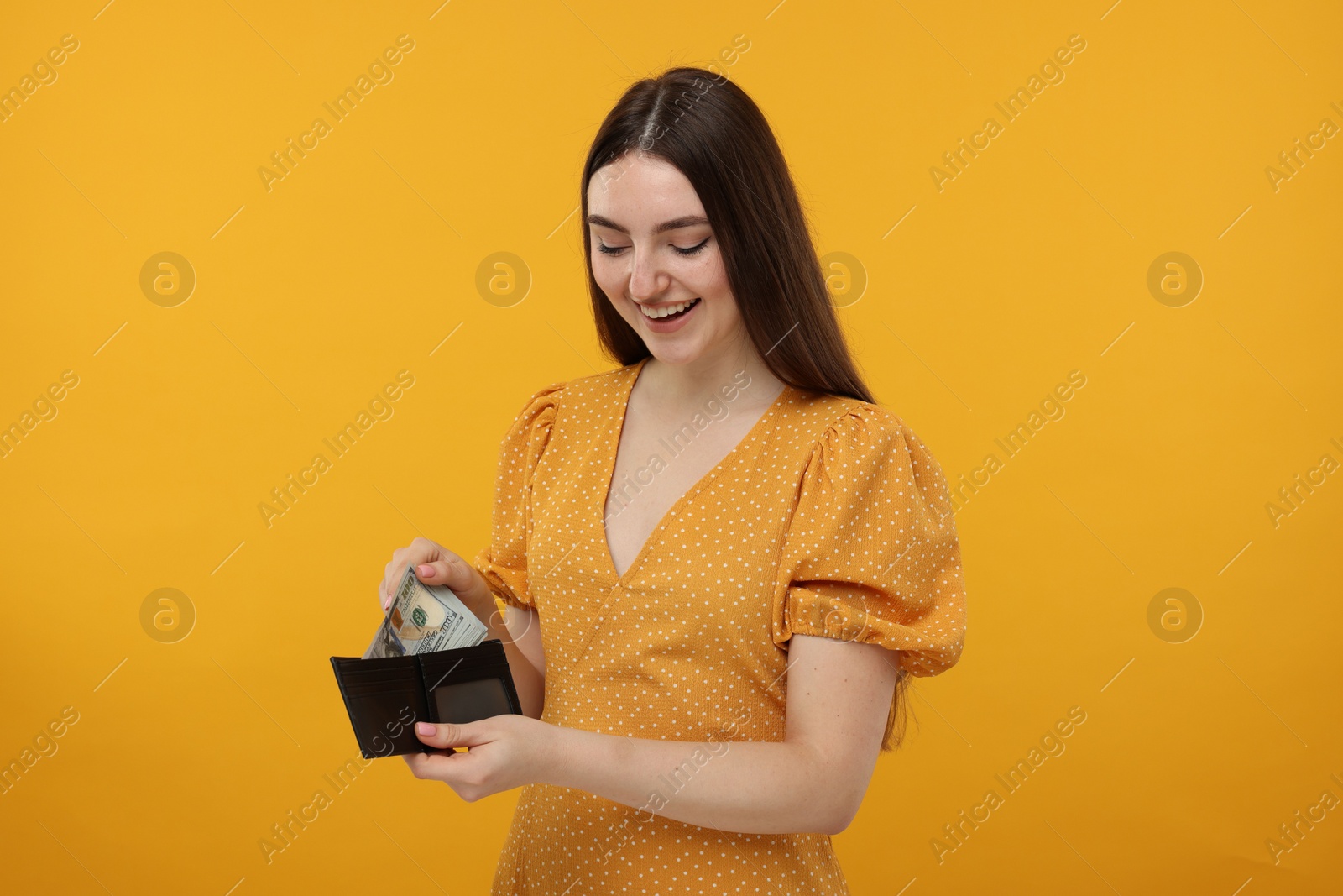 Photo of Happy woman putting money into wallet on orange background