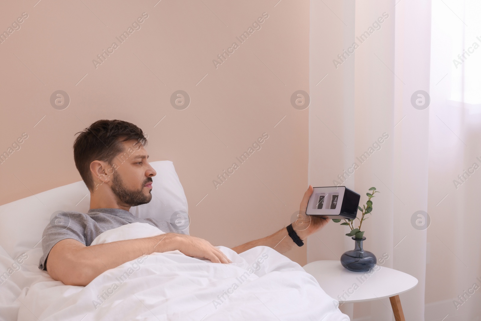 Photo of Sleepy man with alarm clock in bed at home