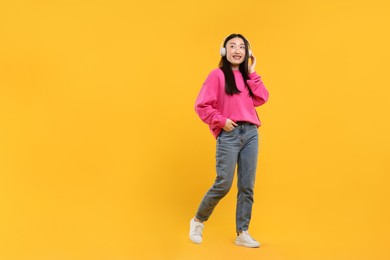 Portrait of smiling woman in headphones on orange background. Space for text