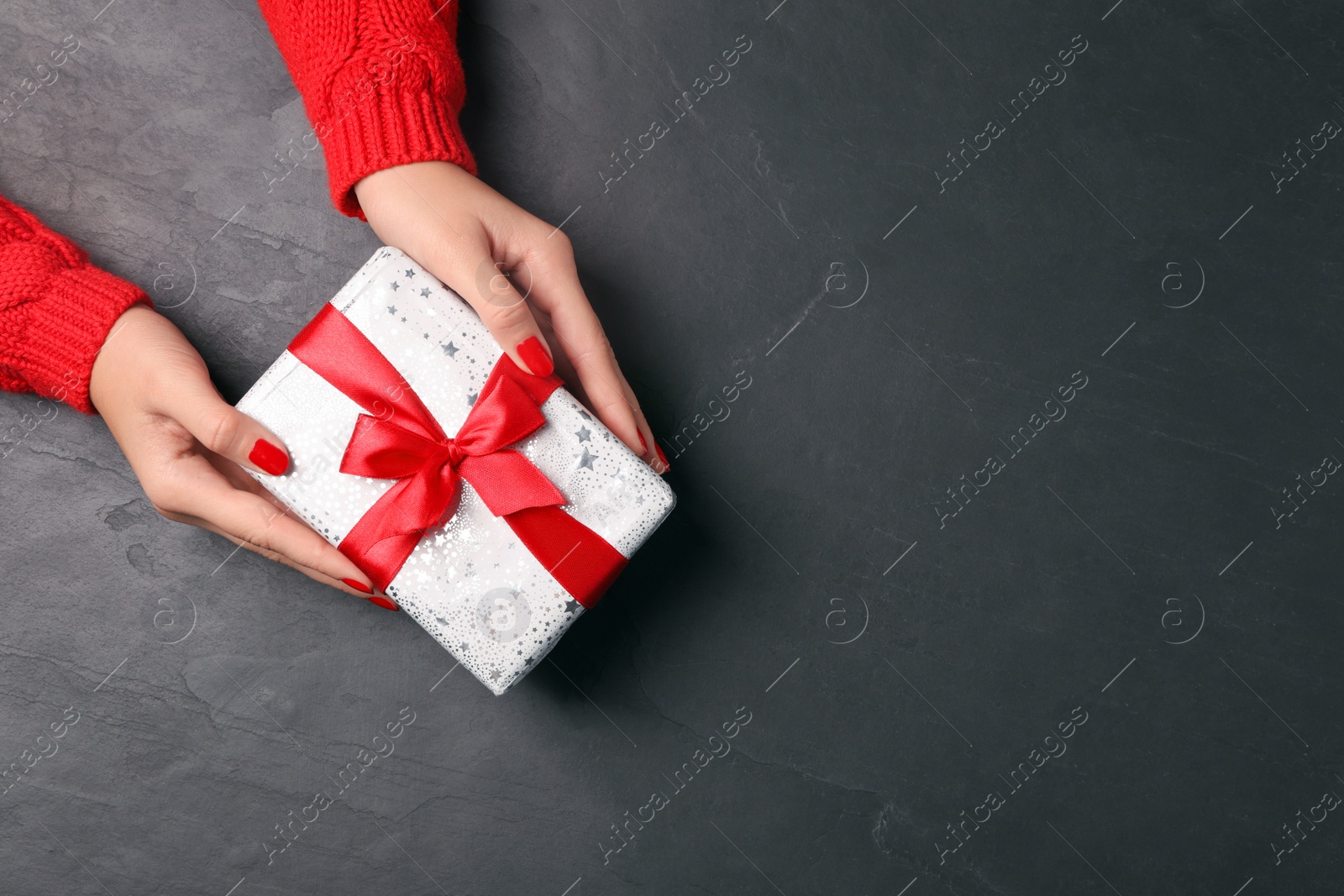 Photo of Christmas present. Woman with gift box at black table, top view. Space for text