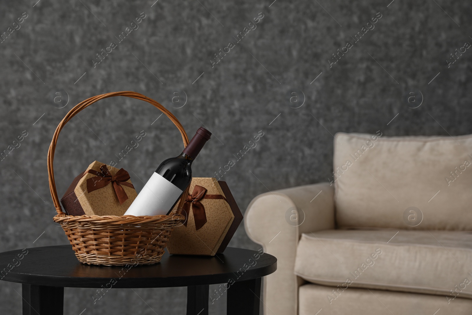 Photo of Wicker basket with bottle of wine and gift boxes on table in room. Space for design