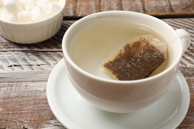 Photo of Tea bag in cup with hot water on wooden rustic table, closeup