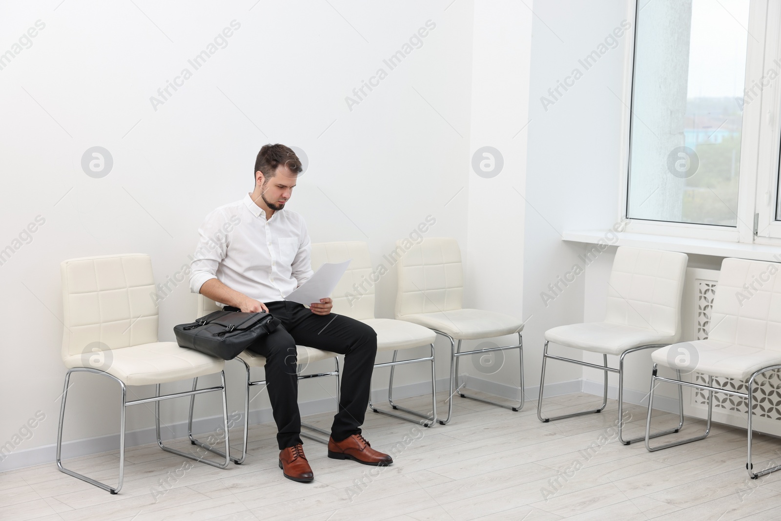 Photo of Man with sheet of paper waiting for job interview indoors