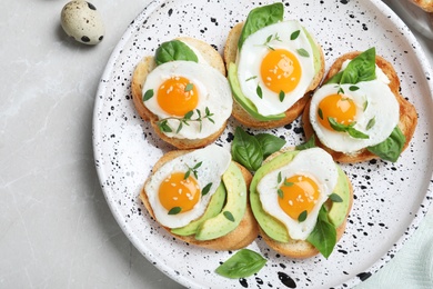 Tasty bruschettas with quail eggs and avocado on light grey marble table, flat lay