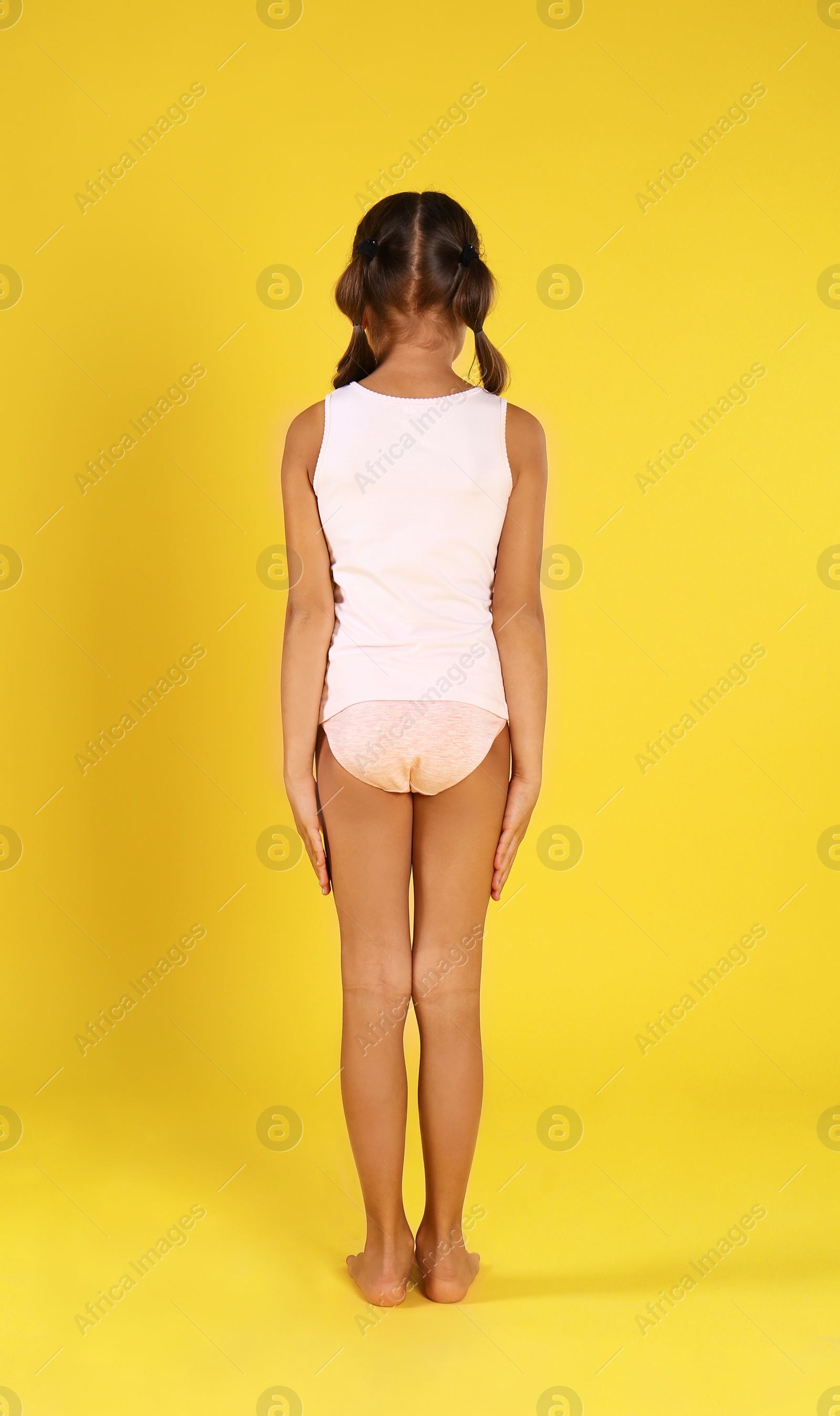 Photo of Little girl in underwear on yellow background, back view