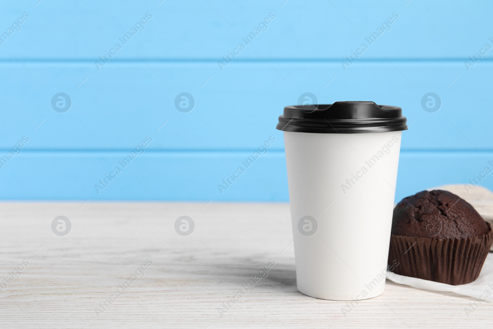 Photo of Paper cup with black lid and muffin on white wooden table, space for text. Coffee to go
