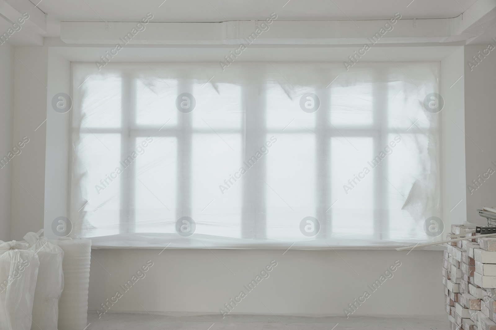 Photo of Windows covered by plastic film and building materials in renovated room