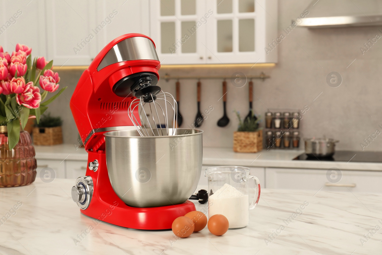 Photo of Modern red stand mixer, eggs and container with flour on white marble table in kitchen