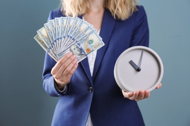 Young businesswoman holding clock and money on color background. Time management