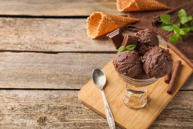 Tasty chocolate ice cream in glass dessert bowl served on wooden table. Space for text