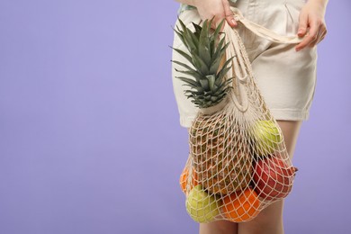 Photo of Woman with string bag of fresh fruits on violet background, closeup. Space for text