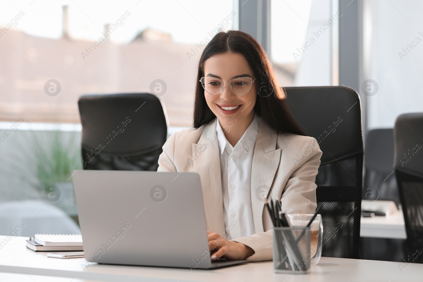 Photo of Happy woman using modern laptop at white desk in office