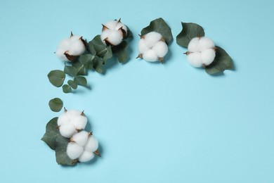 Photo of Cotton flowers and eucalyptus leaves on light blue background, flat lay. Space for text
