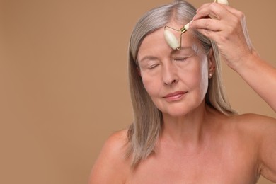 Photo of Woman massaging her face with jade roller on brown background. Space for text