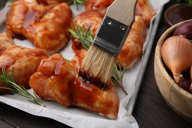 Spreading marinade onto raw marinated chicken wings with basting brush at wooden table, closeup