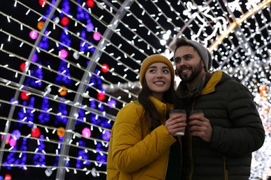 Photo of Lovely couple with cups of hot drinks spending time together at Christmas fair