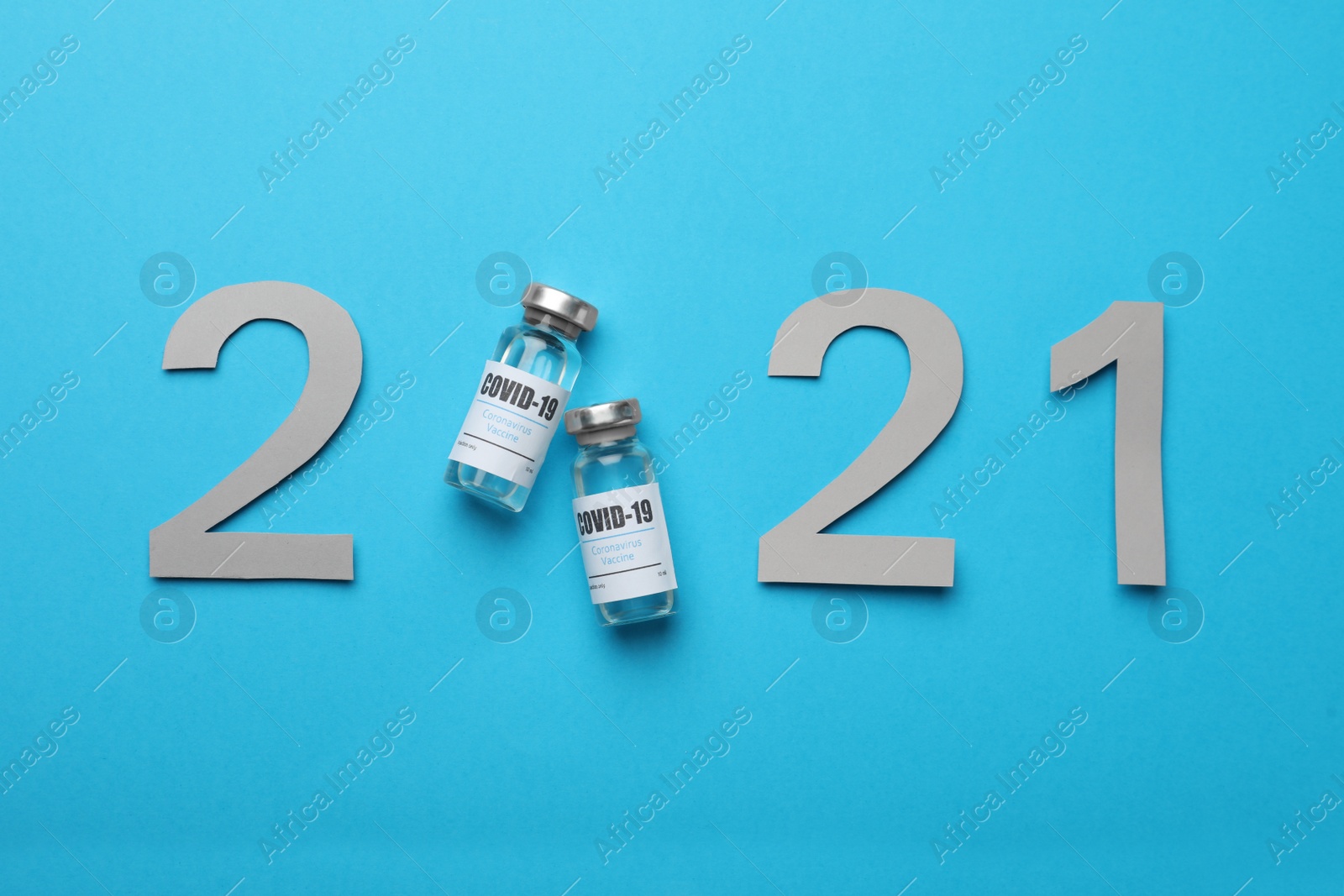 Photo of Paper numbers and vials with coronavirus vaccine forming 2021 on light blue background, flat lay