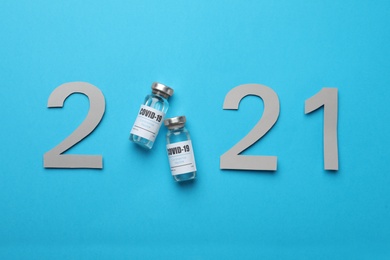 Photo of Paper numbers and vials with coronavirus vaccine forming 2021 on light blue background, flat lay