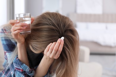 Photo of Upset young woman with abortion pill and glass of water at home