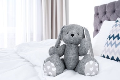 Photo of Cute toy rabbit sitting on bed indoors. Space for text