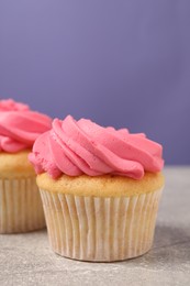 Delicious cupcakes with bright cream on gray table against violet background, space for text