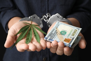 Photo of Woman in handcuffs holding hemp leaf and dollars, closeup