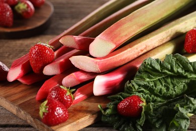 Photo of Cut fresh rhubarb stalks and strawberries on wooden table, closeup