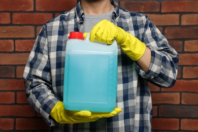 Man in rubber gloves holding canister with blue liquid near brick wall, closeup
