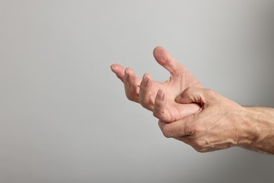 Photo of Arthritis symptoms. Man suffering from pain in hand on gray background, closeup. Space for text