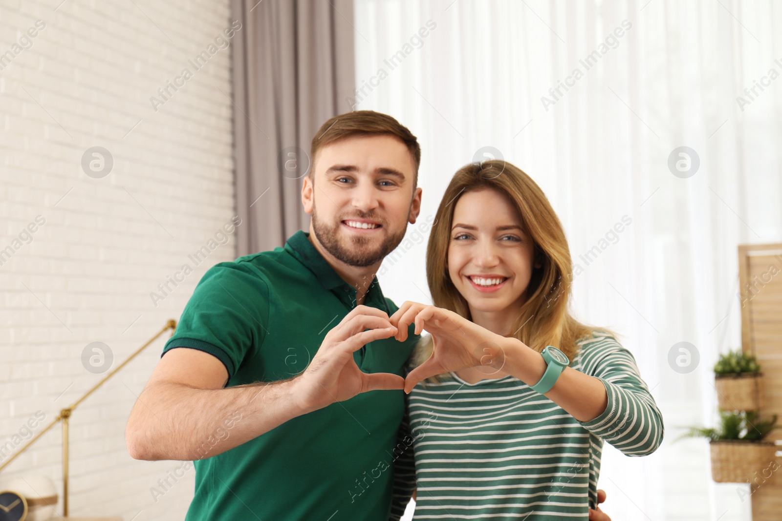 Photo of Happy couple making heart with their hands indoors