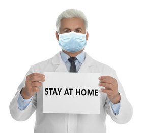 Doctor in medical mask holding sign with text STAY AT HOME on white background