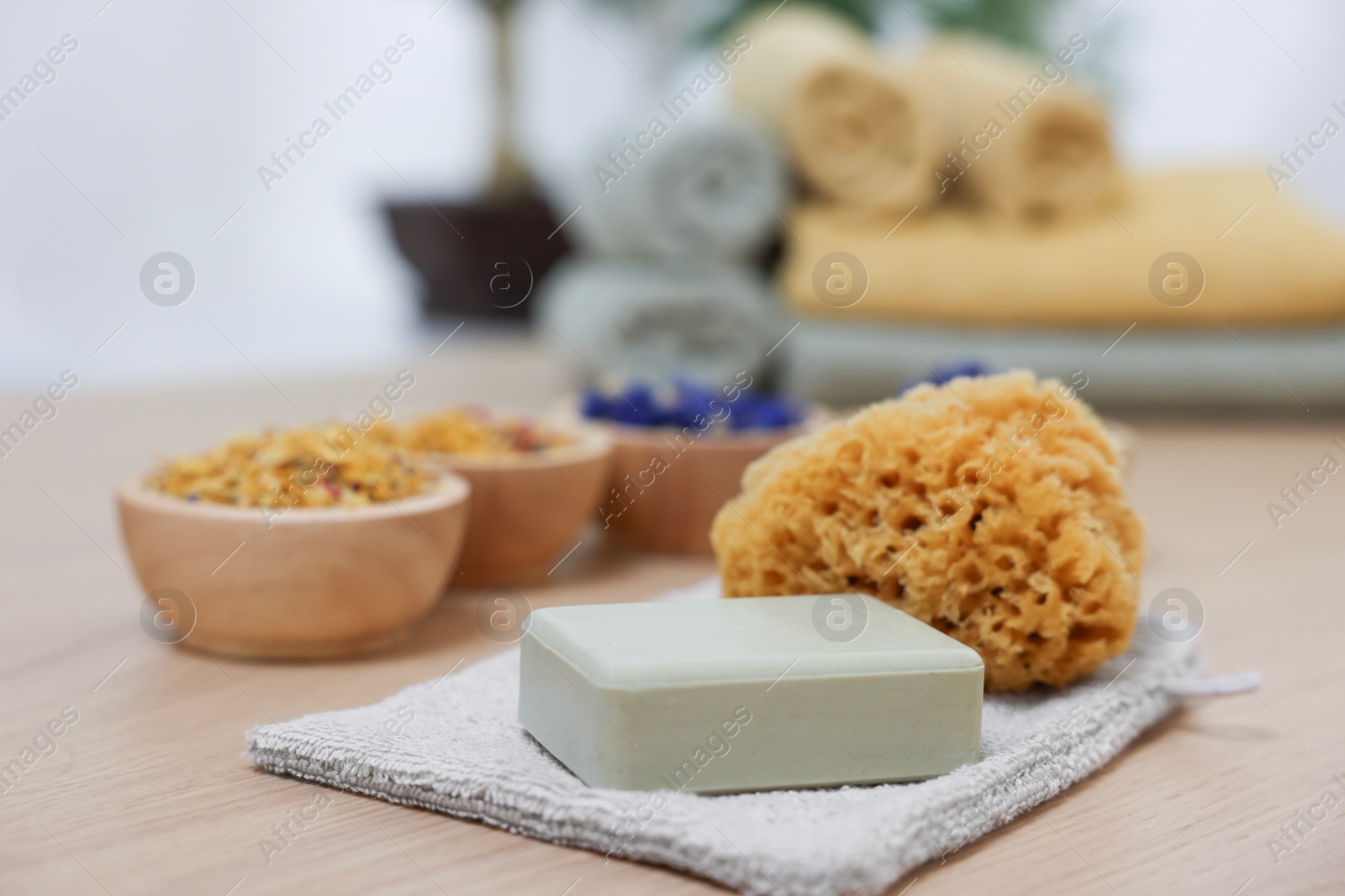 Photo of Soap bar, natural sponge and bowls of dry flowers on light wooden table. Spa therapy