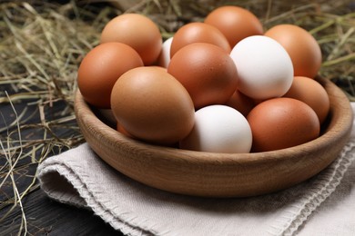 Photo of Fresh chicken eggs in bowl and dried hay on black wooden table, closeup