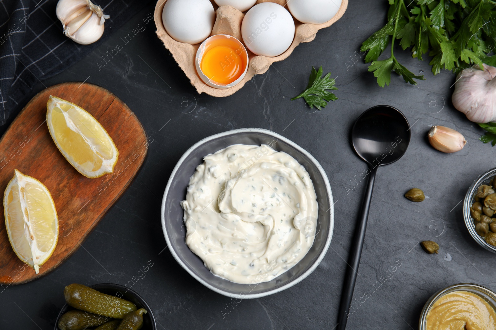Photo of Tasty tartar sauce and ingredients on black table, flat lay