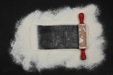 Flour and rolling pin on black table, top view. Space for text