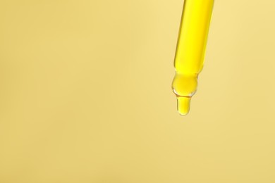 Photo of Dripping serum from pipette on yellow background, closeup. Space for text