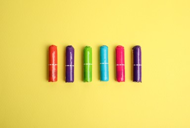 Colorful tampons on yellow background, flat lay