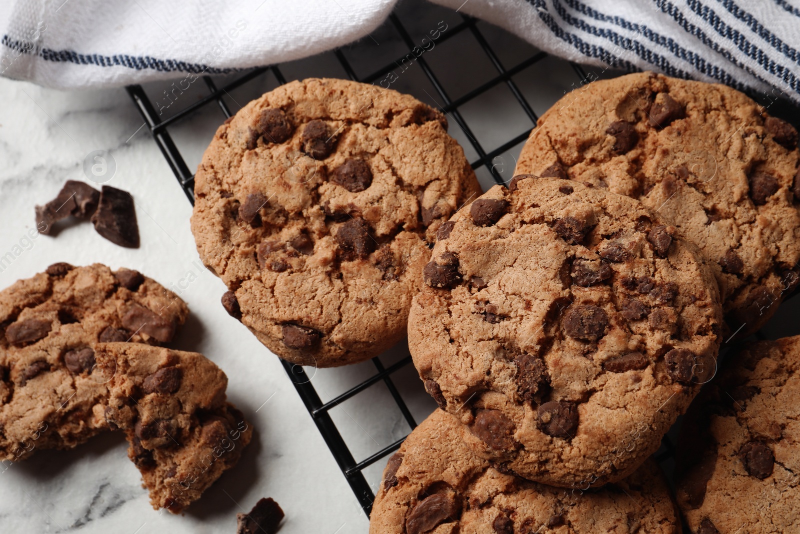 Photo of Cooling rack with delicious chocolate chip cookies on white marble table, closeup