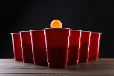 Photo of Plastic cups and ball for beer pong on wooden table against black background