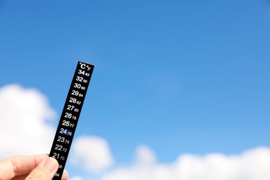 Woman holding weather thermometer against blue sky, closeup. Space for text