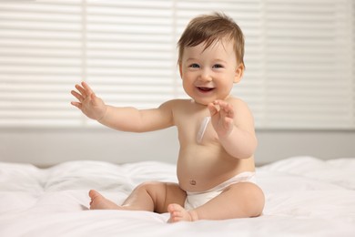 Cute little baby with moisturizing cream onto body sitting on bed at home