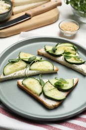 Tasty cucumber sandwiches with sesame seeds and pea microgreens on white table