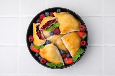 Photo of Bowl with delicious samosas, berries and mint leaves on white tiled table, top view