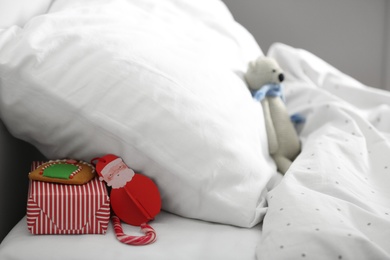Photo of Gift box with candy cane and gingerbread under pillow in children's bedroom. St. Nicholas Day tradition