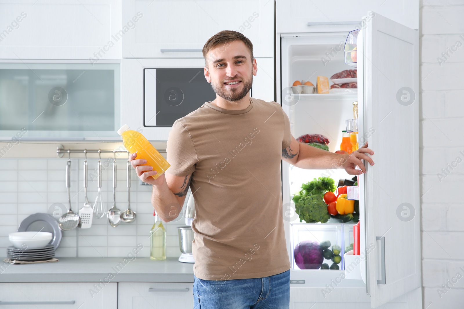 Photo of Man with bottle of juice standing near open refrigerator in kitchen