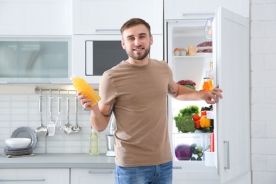 Photo of Man with bottle of juice standing near open refrigerator in kitchen