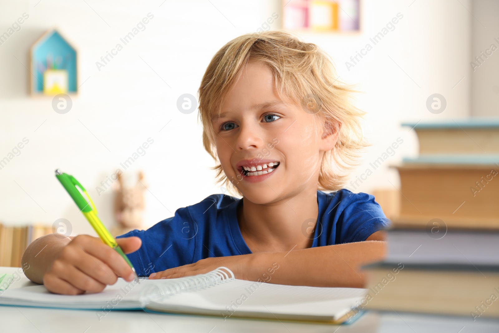Photo of Little boy doing homework at table indoors