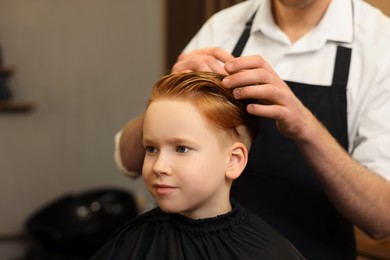 Photo of Professional hairdresser working with boy in beauty salon, closeup